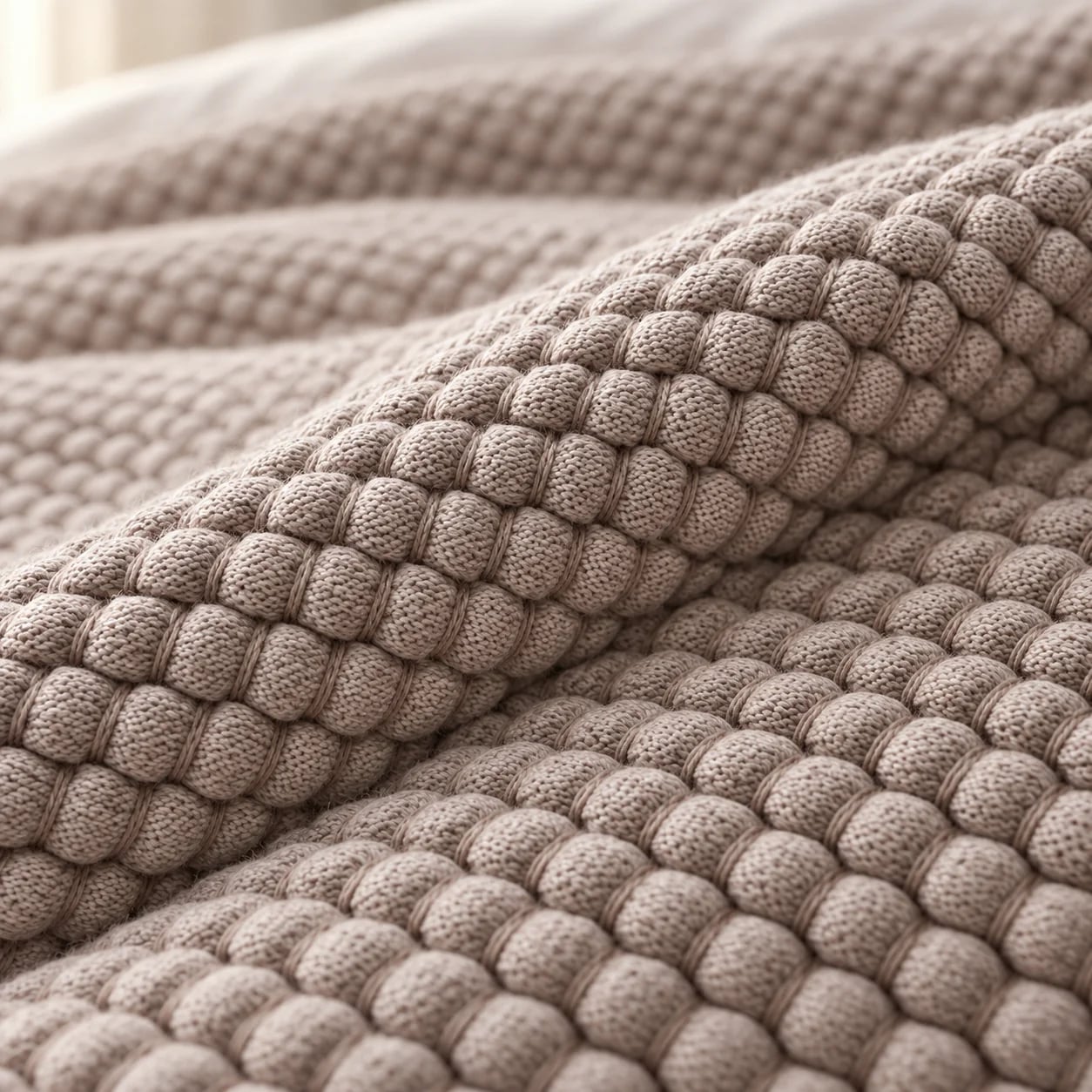 Close detail of an oatmeal bobble-textured coverlet folded across a bed
