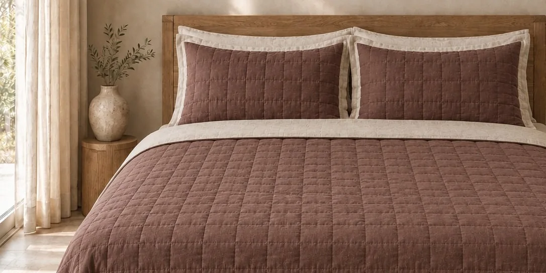 Brown linen quilt set with two flanged pillow shams on a wooden bed